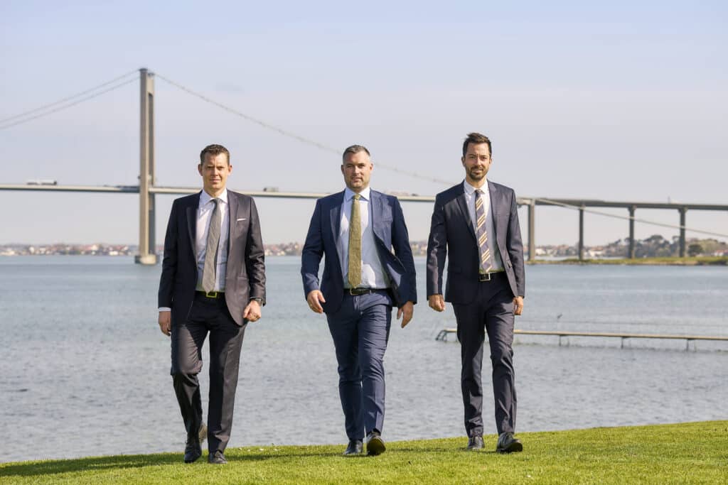 three men walking in front of the little belt bridge